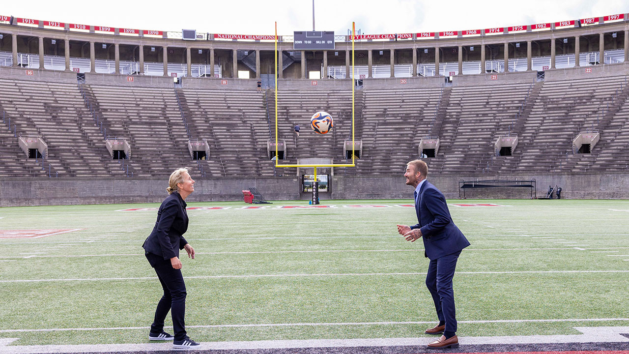 HBS Professor Anita Elberse and Inter Miami owner and soccer legend David Beckham pass a soccer ball back and forth in Harvard Stadium.